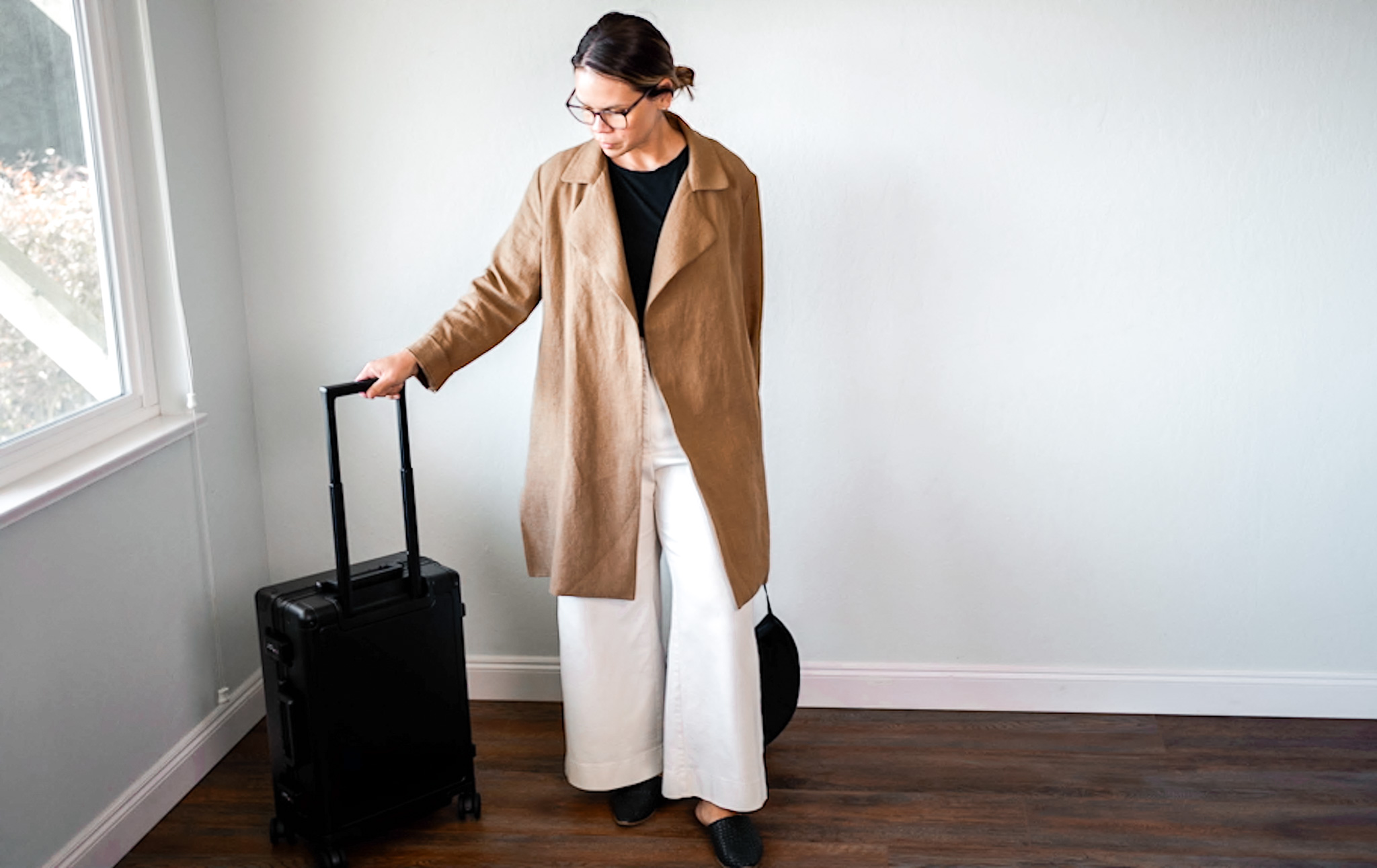 person wearing a long coat next to a suitcase